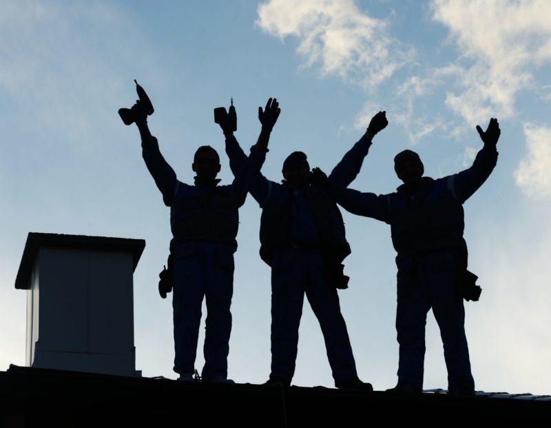 Roofing crew standing on a roof with their arms in the air after finishing a job.