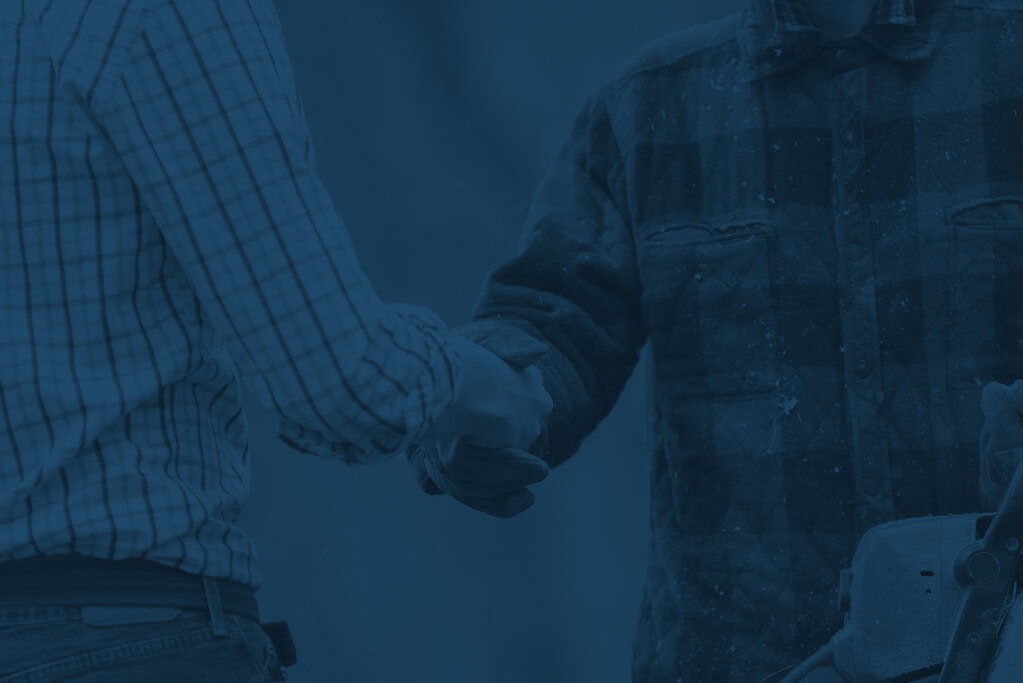One man in formal attire shaking hand of a worker in rugged attire.