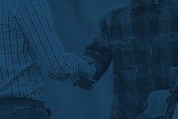 One man in formal attire shaking hand of a worker in rugged attire.
