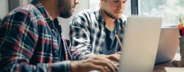 Two men collaborating on roofing CRMs on their laptops