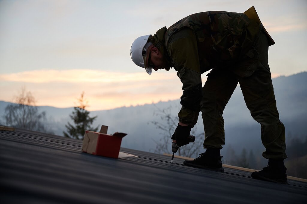 Roofer installing roof, sunset in background