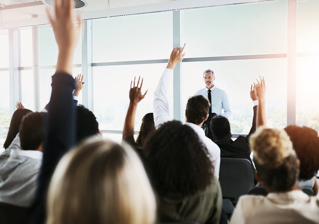 people raising their hands as a man gives a presentation