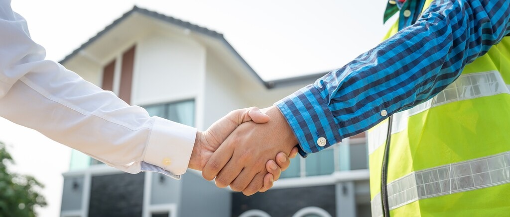 two people shaking hands in front of a home