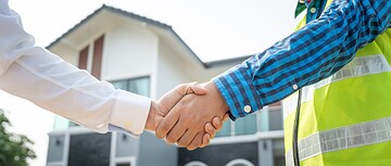two people shaking hands in front of a home